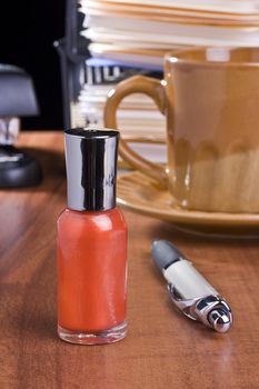 Orange nail polish standing on an office table in front of a cup of coffee.