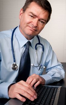 Physician at desk in surgery looks at camera confidently.