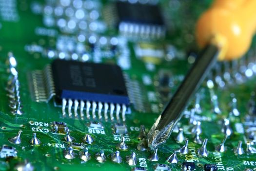 Technician repairing electronic circuit board. Lens zoomed with focus on screwdriver tip.
