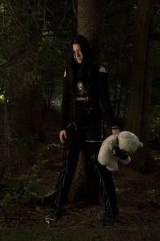 early twenties girl dress in goth fashion with a white teddy bear wearing a gaz mask lost in the woods