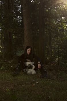 black and white portrait of a twenty something girl dress in goth fashion with a white teddy bear wearing a gaz mask, while being scared lost in the woods