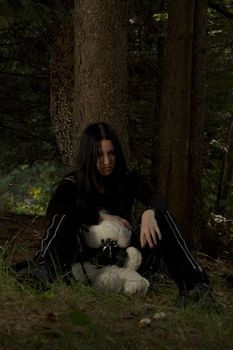 early twenties girl dress in goth fashion with a white teddy bear wearing a gaz mask lost in the woods