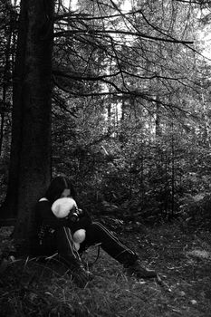 black and white portrait of a twenty something girl dress in goth fashion with a white teddy bear wearing a gaz mask, while being scared lost in the woods