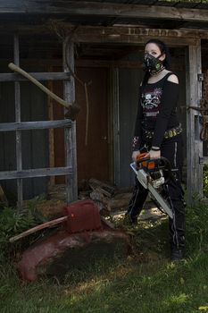 twenty something girl dress in goth fashion with a chainsaw in front of a abandon shack