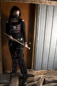 twenty something girl dress in goth fashion with a axe in front of a wooden door 