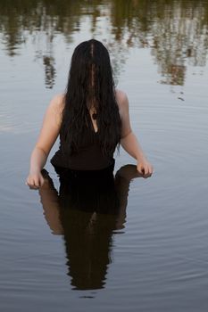 twenty something women with long black hair, wearing a black evening dress, waist deep in a lake at sunset