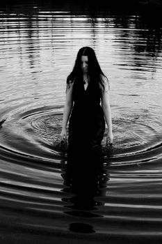twenty something women with long black hair, wearing a black evening dress, walking out of the water