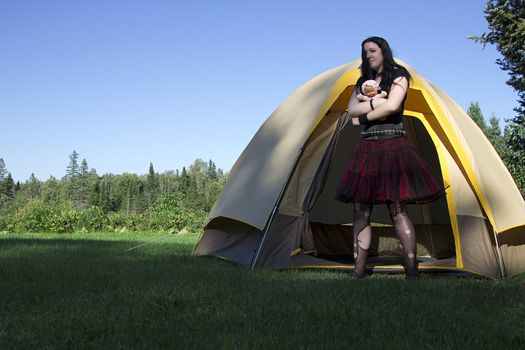 twenty something women wearing goth style clothes and holding a small baby doll coming out of a camping tent