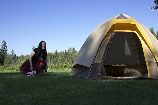 twenty something women wearing goth style clothes and holding a small baby doll pulling on a part of a camping tent