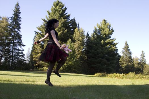 early twenties women wearing goth style clothes and holding a small baby doll running happily in a meadow