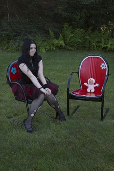 early twenty women wearing goth style clothes sitting on a lawn chair with her baby doll sitting in a lawn chair beside her