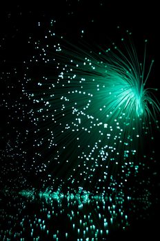 Emerald fibre optic light strands cascading down against a black background and reflecting into the foreground.