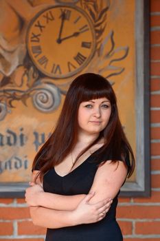 Young, beautiful girl looks at camera on the background of old-time poster with clock.
