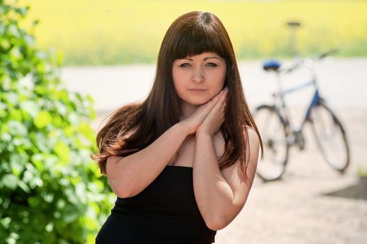 Portrait of young, beautiful girl at summer day with bicycle at the background.
