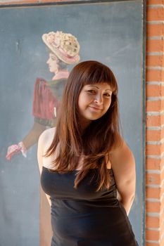 Smiling, young red-haired woman stands in front of old-fashioned drawing.
