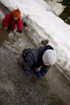 Two small children crewling through muddy water in early spring