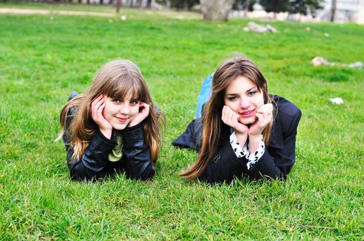    two cheerful teen girls laying on the green grass
