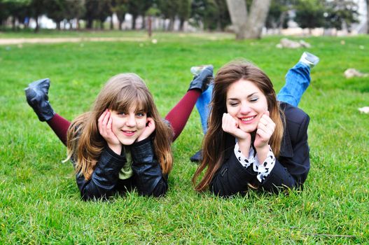 two  laughing  teen girls laying on the green grass 