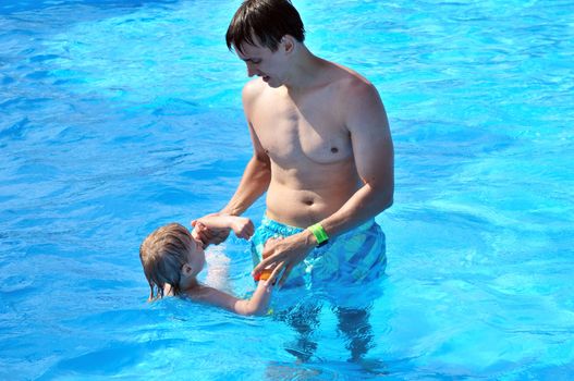 father teaching  his son swimming in water pool 