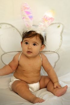 cute baby sitting and smiling with angel wings and colorful bunny ears