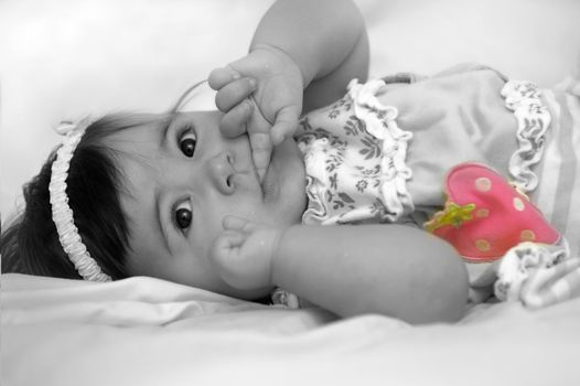 mixed black and white with color photo of baby girl with finger in her mouth and pink strawberry accentuated on her dress