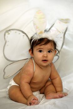 cute baby sitting and smiling with angel wings and colorful bunny ears