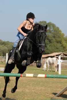 young teenager and her black horse in training of jumping competition