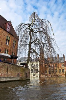 Classic view of channels of Bruges. Belgium. Medieval fairytale city. Summer urban landscape. Tree branches hanging down into the water channel.