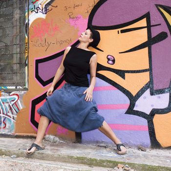 A young woman dancing in front of a wall covered in graffiti