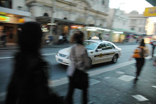 city scene, taxi passing by pedestrians, everything except the taxi is blured