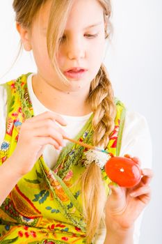 Studio portrait of a young blond girl who is painting an egg red for easter
