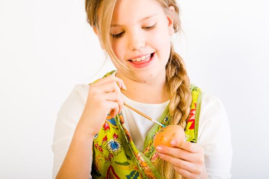 Studio portrait of a young blond girl who ishaving fun painting an easter egg