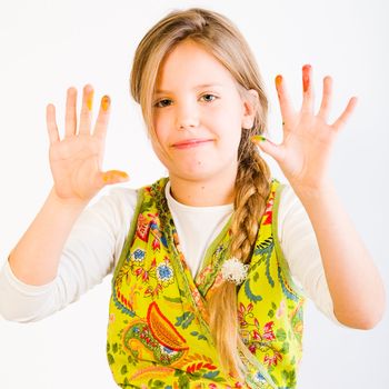 Studio portrait of a young blond girl showing her hands smudged with paint