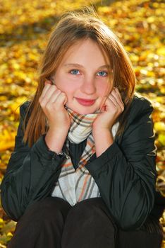 Portrait of a beautiful teenage girl sitting among fallen maple leaves in fall park