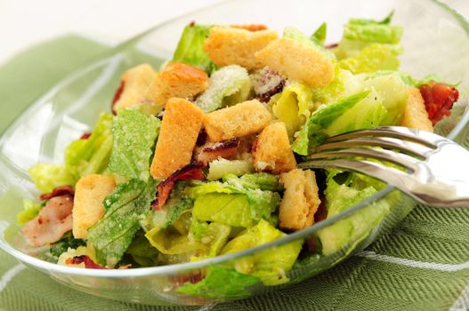 Fresh caesar salad with croutons and bacon bits served in a glass bowl