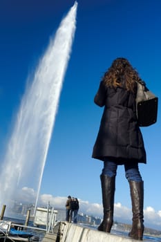 The famous Jet d'Eau fountain in Geneva, Switzerland with tourists admiring it. Taken from a low viewpoint, wide angle.