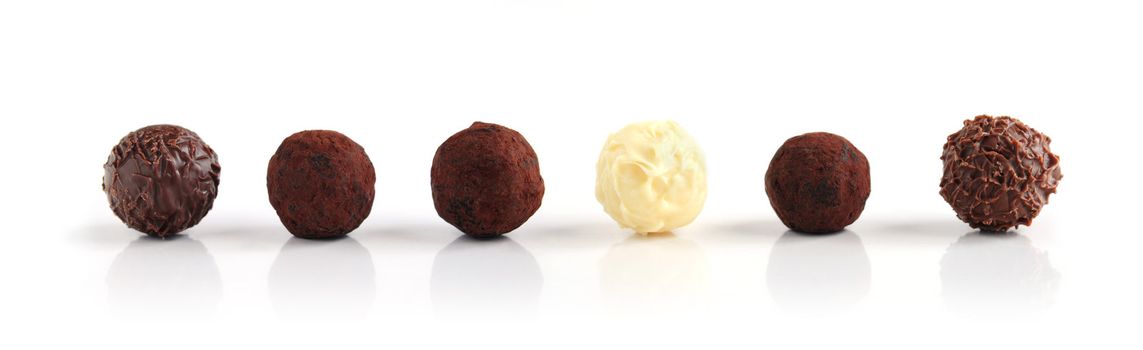 Row of assorted chocolate truffles on white background