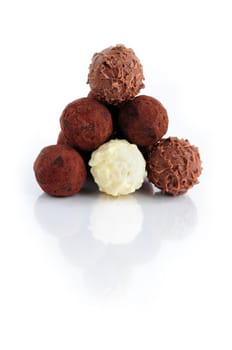 Pyramid of assorted chocolate truffles on white background with reflection