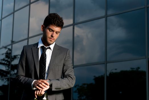 Young businessman looking clock at night on modern building background