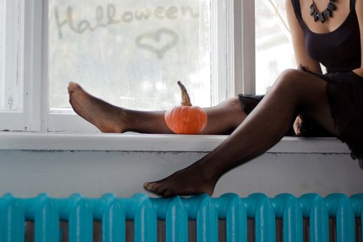 Young lady is seating on the window with small pumpkin