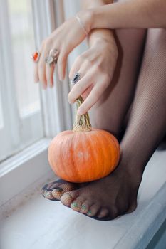 Young lady is seating on the window with small pumpkin