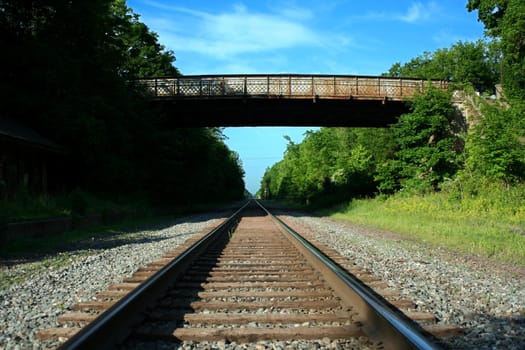 Looking down Railroad tracks with bridge and sky