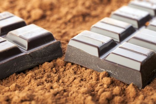 Chocolate bar broken in two pieces on cocoa powder.