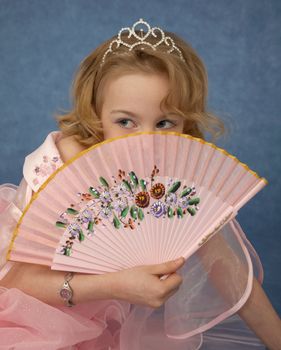 Beautiful girl hides behind her fan on blue