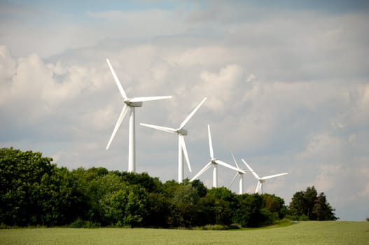 Landscape with green field and cloudscape. In the background you can see five wind turbines.