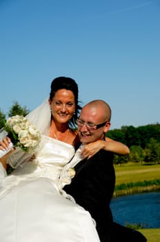 Groom is lifting his bride up in a park.