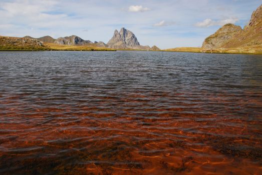 Transparante water of Anayet lake looks red taking the colour of bottom in focus,   Its Aragon, Spain. Beautyful peak du Midi d'Ossau in French site of Pytenees is at background 