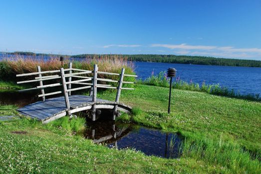 Small wooden bridge in green surroundings of Suomussalmi in the border of Kiantajarvi lake, located in the north of Kainuu  region in Finland