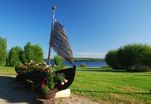 Small wooden boat decorated with flowers is along wolk pass  in green surroundings of Suomussalmi, in the border of Kiantajarvi lake, located in the north of Kainuu  region in Finland