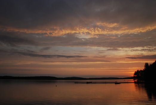 sunset at beutiful lake Kuuhankavesi in Central Finland, there are people on the wooden foot-pass of Ruokoniemi camping in Hankasalmi village, the hidden sun is  coloring sky and water in red